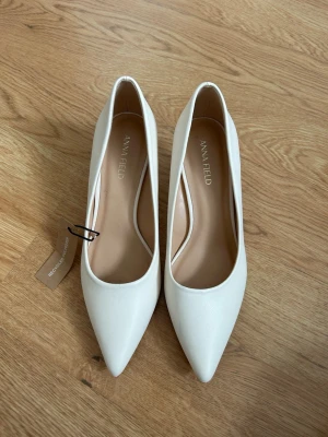 Vita Klackar från Anna Field - Snygga vita klackar från Anna Field med spetsig tå. Skorna har en stilren design i slätt material och en klassisk siluett som passar perfekt till student, bal osv. Helt oanvända med lappen kvar. Storlek 38💞