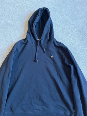 Mörkblå hoodie med broderad logga - Snygg mörkblå hoodie från Morris med broderad vit logga på bröstet. Klassisk modell med huva och dragsnören samt ribbade muddar vid ärmar och nederkant. Tillverkad i mjuk bomull för skön känsla. Perfekt för en avslappnad och stilren look.