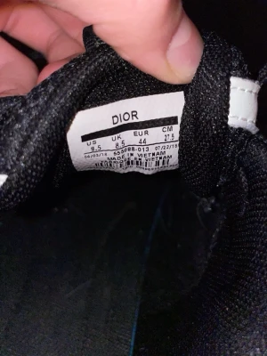 Svarta Dior sneakers med reflexdetaljer - Snygga svarta sneakers från Dior med vita och reflekterande detaljer. Skorna har en sportig design med mesh och läderpaneler, samt snörning framtill. Perfekta för dig som vill ha en exklusiv och trendig look.