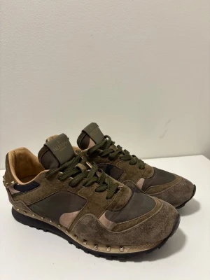 Valentino rockrunners - Snygga sneakers från Valentino i olivgröna och bruna toner med mockadetaljer och coola nitar runt hälen. Skorna har gröna skosnören, svart sula och beige insida. Perfekt för dig som gillar streetstyle och exklusiva detaljer. Saknar endast en nit. Passar stort.