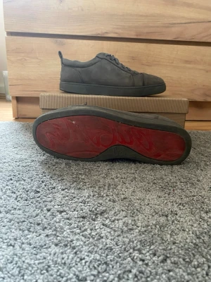 Grå sneakers från Christian Louboutin - Snygga grå sneakers från Christian Louboutin med klassisk röd sula. Skorna har en låg profil, rund tå och är tillverkade i mocka. Perfekta för dig som vill ha en clean och exklusiv look.
