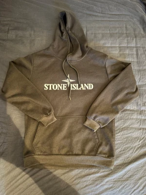 Svart hoodie från Stone Island - Pris går att diskutera. Snygg svart hoodie från Stone Island med stor logga och kompass på bröstet. Klassisk känguruficka framtill och justerbar huva med dragsko. Tillverkad i mjukt bomullsmaterial som är skönt att bära. Perfekt för dig som gillar streetwear och vill ha en stilren look. 