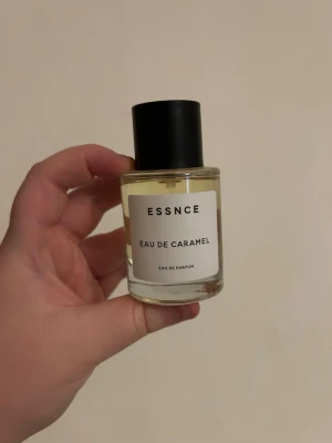 ESSNCE Eau de Caramel parfym - ESSNCE Eau de Caramel är en Eau de Parfum i en rund glasflaska med svart lock. Doften har en söt karamellton och flaskan har en minimalistisk vit etikett med svart text. Perfekt för dig som gillar gourmanddofter och stilren design.
