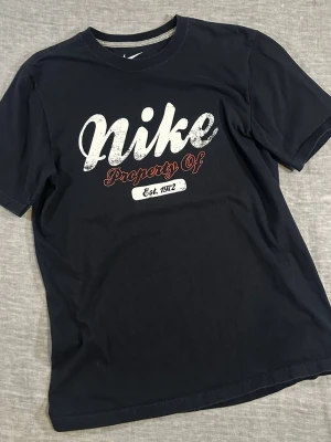 Nike Vintage Printout Graphic Tee Black Cotton T-Shirt Size L - Nike vintage printout graphic tee “Property Of” Est. 1972 in black. Clean athletic look with distressed style logo for that vintage vibe. Easy everyday piece for streetwear or casual fits. Labeled L.  Measurements: P2P 50.5 cm, waist 51.5 cm, S2S 44 cm, length 70 cm. Good used condition, no major flaws.