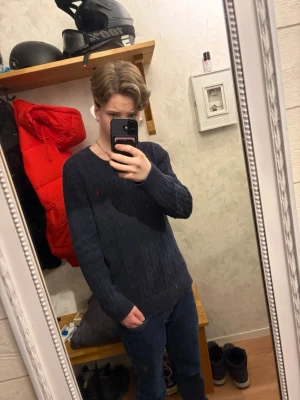 Mörkblå stickad tröja från Ralph Lauren - Säljer en mörkblå stickad tröja från Ralph Lauren med klassiskt kabelstickat mönster och liten röd logga på bröstet. Tröjan har rund halsringning och långa ärmar. Perfekt för dig som gillar stilrena och tidlösa plagg. Original pris~ 2595kr, priset är inte hugget i sten. Skriv om ni undrar något!