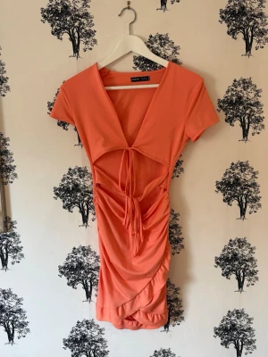 Korall kortklänning med snörning - Trendig korallfärgad kortklänning från Shein med v-ringning, snörning framtill och rynkade detaljer längs kjolen. Klänningen har korta ärmar och är tillverkad i ett mjukt, stretchigt syntetmaterial som sitter snyggt på kroppen. Har en fläck som syns på sista bilden men det är absolut inget man tänker på när den sitter på!💓🌸