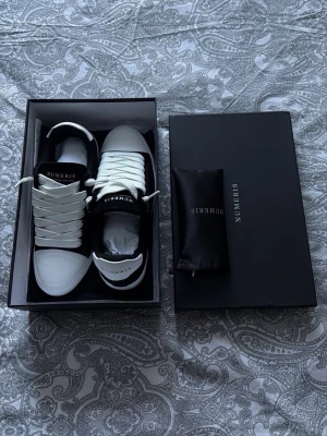 Svarta sneakers från Numeris - Snygga sneakers från Numeris i svart mocka med vita detaljer och grov sula. Skorna har vita skosnören, vit tå och häl i strukturmaterial samt kontrastsömmar. Klassisk låg modell med logga på plösen. Perfekta för en trendig streetwear-look. Helt nya aldrig använda, box o extra snören tillkommer. 