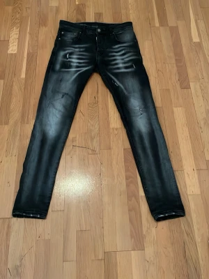 Svarta DSOUA jeans med slitningar  - Säljer ett par svarta skinny jeans med coola slitningar och blekta detaljer över låren. Jeansen har klassisk femficksmodell, knappgylf och smal passform. Perfekta för dig som gillar en edgy streetstil.