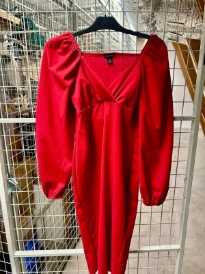 Röd långärmad klänning från Bohoo - Trendig röd klänning från Bohoo med puffiga långärmar och v-ringad omlottdesign. Klänningen har en figurnära passform och är perfekt för dig som vill sticka ut. Tillverkad i mjukt material som känns bekvämt mot huden.