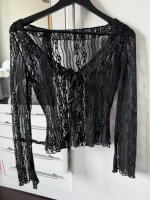 Svart spetstopp med snörning - Säljer en svart spetstopp med långa ärmar och v-ringning. Blusen har snygg snörning framtill och är croppad i modellen. Från shein