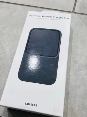 Samsung Super Fast Wireless Charger Duo - Trådlös laddare från Samsung med plats för två enheter samtidigt. Laddaren är svart och har en stilren, rektangulär design i plast. Perfekt för dig som vill ladda både mobil och hörlurar samtidigt utan sladdar.