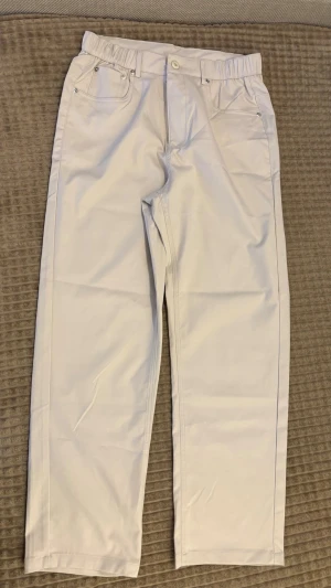 Creme raka chinos med resårmidja  - Säljer ett par creme chinos med rak passform och resår i midjan. Byxorna har klassiska fickor fram och bak, bälteshällor och stängs med knapp och dragkedja. Perfekta för en clean och stilren look. Materialet känns mjukt och lätt.