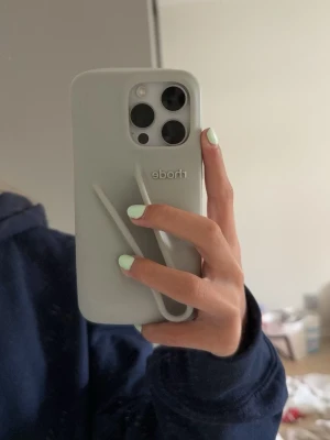 Ljusgrått Rhode mobilskal - Snyggt ljusgrått mobilskal från Rhode❣️Skalet är gjort för iPhone 13 Pro (visas på bild 3) men passar även rätt så bra på min nya mobil iPhone 16 pro (den vita mobilen på bild 1). Skalet är i väldigt bra skick och köptes förra sommaren från Rhodes egna hemsida.💄📱❣️