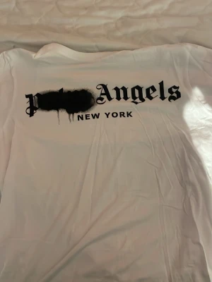 Vit t-shirt från Palm Angels - Säljer en vit t-shirt från Palm Angels med stor svart logga och texten 'New York' på bröstet. T-shirten har klassisk passform och är gjord i mjuk bomull. Perfekt för dig som gillar streetwear och vill ha en clean look med statement-tryck