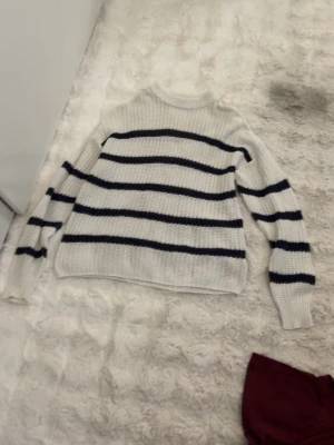 Vit stickad tröja med svarta ränder - Säljer en vit stickad tröja med svarta horisontella ränder. Tröjan har rund halsringning, långa ärmar och ribbade muddar. Perfekt för en avslappnad och stilren look. Ifrån lager 157