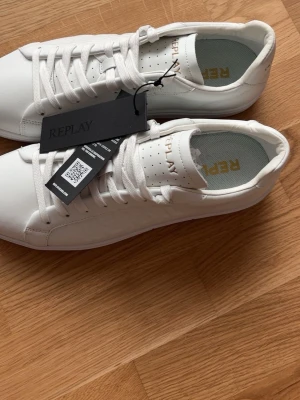 Vita låga sneakers från Replay - Stilrena vita sneakers från Replay med klassisk låg profil och vita snören. Skorna har diskret Replay-logga på plösen och är tillverkade i slätt syntetmaterial. Perfekta för en clean och modern look. Köpta för 1500kr men säljer då jag aldrig använt dom