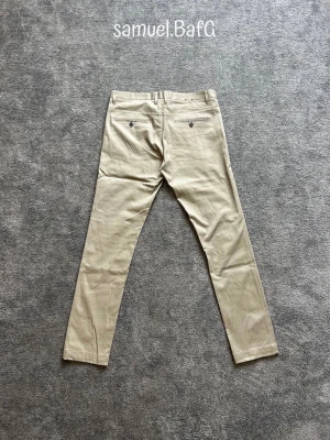 Riley Stanton Chinos - Säljer ett par fina Beigea Riley Stanton Chinos som funkar perfekt för en lite finare tillställning. Storlek 50 (ungefär W34/L32). Snygg blå inner lining och klassisk chinos-design.