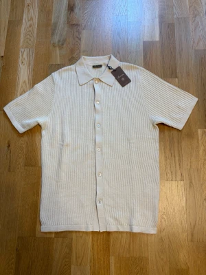 Beige ribbad skjorta från Stenströms - Stilren beige skjorta från Stenströms med korta ärmar och ribbad struktur. Skjortan har klassisk krage och knäppning framtill. Perfekt för dig som gillar en clean och modern look.