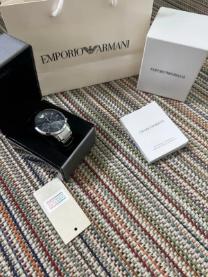 Emporio Armani silverfärgad klocka blå - Stilren klocka från Emporio Armani med silverfärgad länk i metall och mörkblå urtavla. Klockan har kronograf-funktion, datumvisning och tydliga indexmarkeringar. Levereras i originalask med manual och tagg.