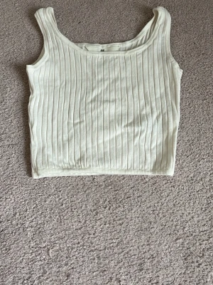 Vit ribbad linnetopp från H&M - Snygg vit ribbad linnetopp från H&M med breda axelband och croppad passform. Perfekt till jeans eller kjol för en enkel och fräsch look. Materialet är mjukt och stretchigt för extra komfort.