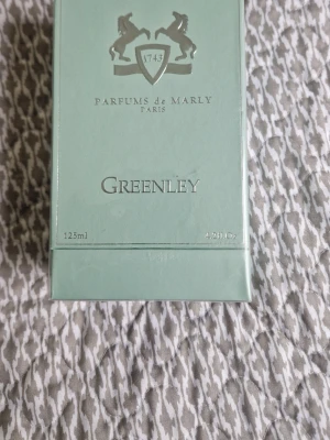 Parfums de Marly Greenley 125ml - Greenley från Parfums de Marly är en exklusiv Eau de Parfum i en stilren, ljusgrön kartong med silverdetaljer. Förpackningen rymmer 125 ml och har en elegant design med märkets logotyp och text i silver. Tillverkad i Frankrike.