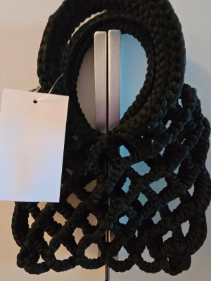  H&M Liten handväska Svart nätväska - svart handväska med flätad nätstruktur och runda handtag. Väskan är tillverkad i tjockt, flätat repmaterial. Mått: Bredd ca 17 cm Längd ca 22 cm  Mått finns  med på bilderna   Material:  93% Polyester  7%   Elastan