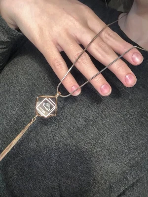 Geometriskt halsband med kristall - Unikt halsband med en lång kedja i guldfärg och ett geometriskt hänge i form av en kub med en klar kristall inuti. Hänget har även en dekorativ tofs i metall. Lite rostig men inget som syns på håll!