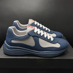 Prada Cups - Snygga sneakers i blått och grått med vit sula och vita skosnören. Ovandelen är i mesh och syntetmaterial för en sportig look. Röd detalj på plösen ger extra stilpoäng. Perfekta för dig som gillar en modern och clean stil. Nypris ~6 tusen