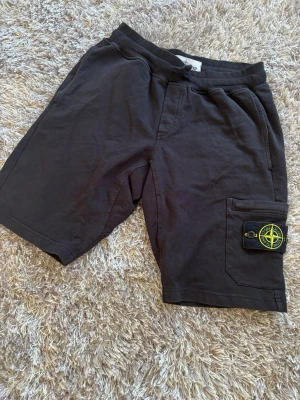 Svarta shorts från Stone Island - Svarta shorts från Stone Island med klassisk logotyp-patch på benfickan. Modellen har normal passform, elastisk midja och är tillverkad i mjuk bomull. Perfekta för en avslappnad och stilren look.