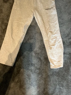 Grå och svarta mjukisbyxor Jack & Jones M - Säljer ett par ljusgrå och svara mjukisbyxor från Jack & Jones Pants Studio. Byxorna har resår i midjan och är tillverkade i mjukt, skönt material. Diskret tryck med texten 'Originals Studio' på ena benet. Perfekta för chill dagar hemma. Man får båda vid köp!
