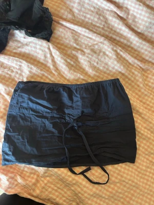 Mörkblå kortkjol från Editheaf - Mörkblå tubtopp från Editheaf med elastisk midja och snörning framtill. 