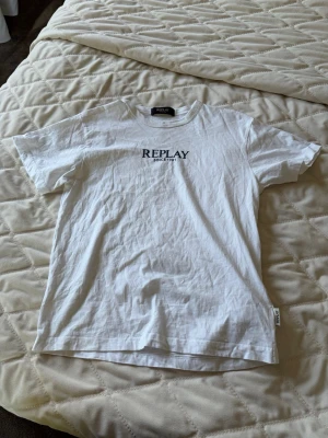 Vit t-shirt från Replay - Snygg vit t-shirt från Replay med svart tryck 'REPLAY SINCE 1981' på bröstet. Klassisk rund halsringning och korta ärmar. Perfekt basic-plagg i mjuk bomull som funkar till allt.