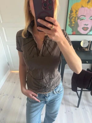 Brun kortärmad topp med krage - Snygg brun topp med korta ärmar och krage. Toppen har ett unikt mönster och en liten v-ringning framtill. Tillverkad i bomull. I fint skick. 