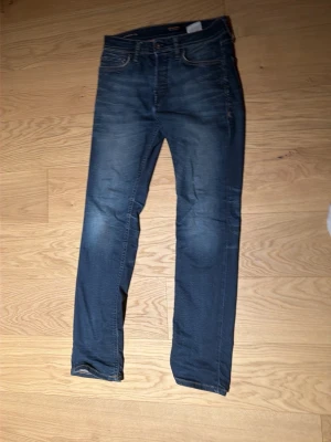 Mörkblå slim fit jeans - Snygga mörkblå slim fit jeans med lätt slitningar framtill och klassiska fem fickor. Jeansen har normal midja och raka ben. Perfekta för en avslappnad och trendig look. Materialet är troligtvis bomull med lite stretch för extra komfort.