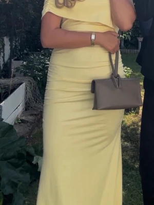 Ljusgul långklänning med offshoulder - Snygg ljusgul långklänning med offshoulder och figurnära passform. Klänningen har en enkel och elegant design med lätt rynkade detaljer längs sidorna. Perfekt för sommarens alla tillfällen. har slitage längst ner men inget man tänker på! är 175 till referens!