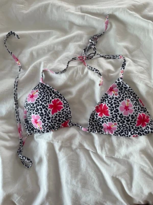Blommig och leopardmönstrad bikini - Snygg trekantsbikini med svartvitt leopardmönster och rosa samt röda blommor. Bikinin har knyt i nacken och ryggen för justerbar passform. Perfekt för sommardagar på stranden. Kommer med vaddering i 