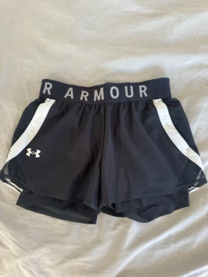 Svarta träningsshorts från Under Armour - Snygga svarta träningsshorts från Under Armour med inbyggda cykelbyxor och fickor. Storlek XS.