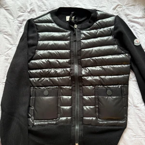 Svart Cardigan från Moncler - Snygg svart cardigan från Moncler med stickade ärmar och dragkedja framtill. Perfekt för lite varmare dagar nu när våran kommer och du vill hålla stilen. 🤩Säljer då den tyvärr var för liten. I storlek S, mitt pris 4899 pris kan diskuteras vid snabb affär ! ❣️Nästan helt oanvänd och såklart äkta! den enda deffekten som finns är att lappen man kan hänga den med på en galge exempelvis är sönder men inget man tänker på