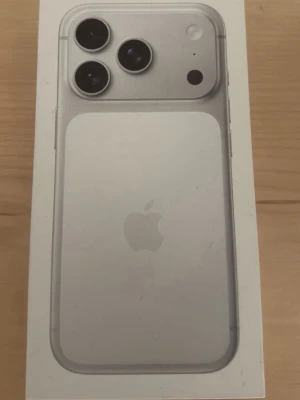 Iphone 17 pro 256 gb 98 procent batterihälsa - Snygg silverfärgad iPhone med stilren design och tre kameror på baksidan. Telefonen har platt ram i metall och glasbaksida med Apple-loggan. Perfekt för dig som gillar modern teknik och vill ha en mobil med grym kamera.