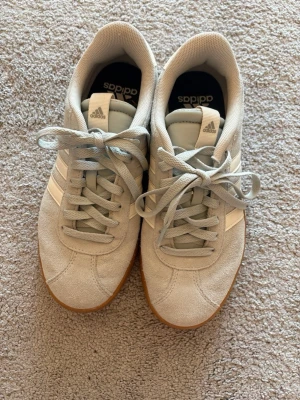 Adidas ljusgröna sneakers  - Snygga ljusgröna sneakers från Adidas med klassiska vita ränder på sidan. Ovandelen är i mockaliknande material och skorna har låga skaft. Perfekta för en clean och sportig look.