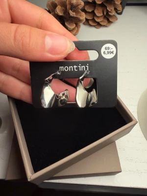 Silvriga chunky örhängen Montini - Säljer ett par silvriga chunky örhängen från Montini. De har en cool, vågig och abstrakt form som verkligen sticker ut. Perfekta för dig som gillar statement-smycken och vill addera lite edge till din look. Stiftet är i metall och örhängena är blanka och moderna.