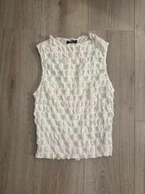 Vit ärmlös linnetopp från Gina Tricot - Säljer en vit ärmlös linnetopp från Gina Tricot. Toppen har en strukturerad, rynkad yta som ger en cool och trendig look. Perfekt att styla till jeans eller kjol för en fräsch sommaroutfit.
