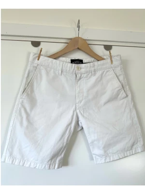 Bondelid - Vita chinos shorts - storlek S - Stilrena vita chinos shorts från Bondelid i storlek S (size 31 i deras egna storlek). Den populära Sebastiano-modellen med raka korta ben, fickor fram och bak och diskret logo-brodyr bak. Finvävt material i 100% bomull, så bra material som andas. Perfekta för en avslappnad men stilren look under varmare dagar. Mycket gott skick, som nya!