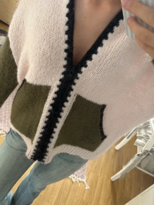 viral rosa\grön Zara tröja - Säljer en stickad kofta med dragkedja. Koftan är ljusrosa med olivgröna ärmar och detaljer samt svarta kanter längs dragkedjan. Materialet ser ut att vara mjukt och lite luddigt, perfekt för kyliga dagar. Klassisk ribbstickning vid ärmslut och nederkant. Har en blå bläck fläck på insidan, som inte är synlig.