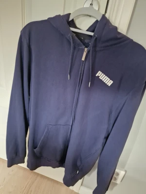 Mörkblå zip hoodie från Puma - Snygg mörkblå hoodie från Puma med dragkedja framtill och vit logga på bröstet. Perfekt för en avslappnad och sportig stil.