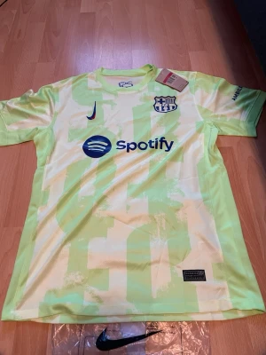 Gul Barcelona matchtröja Nike - Snygg gul Barcelona matchtröja från Nike med klubbmärke och Spotify-logga på bröstet. Tröjan har korta ärmar, rund hals och ett unikt mönster i ljusgult. Tillverkad i lätt och ventilerande material, perfekt för träning eller match.