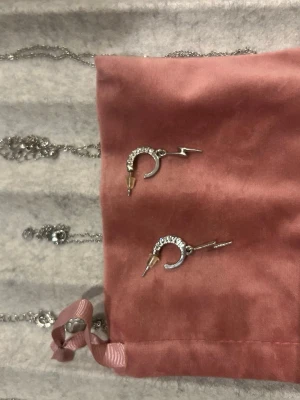 Silvriga örhängen med blixt och stenar - Säljer ett par silvriga örhängen i form av halvmånar dekorerade med små gnistrande stenar och en cool blixtdetalj. Örhängena har även en liten guldfärgad spets i änden för extra edge. Perfekta för dig som gillar unika accessoarer.