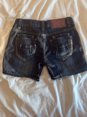 Mörkblå jeansshorts med kontrastsömmar - Snygga mörkblå jeansshorts med slitningar och kontrastsömmar. Midjemått: 35cm, Gren: 18cm