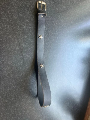 Svart bälte med stjärndetaljer - Snyggt svart bälte i skinn med coola silverfärgade stjärnor längs remmen. Perfekt accessoar för att lyfta din outfit med en edgy touch. Klassisk metallspänne och stilren design.