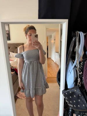 Randig offshoulder klänning - Söt sommarklänning med svarta och vita ränder. Offshoulder-modell med volangdetalj vid ärmar och nederkant. Klänningen har en luftig passform och är perfekt för varma dagar. Tillverkad i ett lätt och bekvämt material.